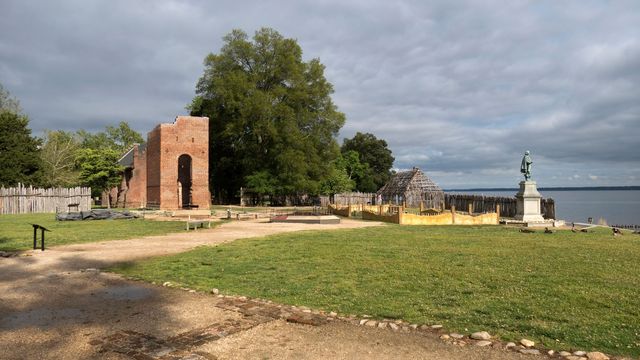 The James River flows past the 1611 Councillor's Row building foundation as sunlight shines on the 1686 Historic Tower and John Smith statue at the James Fort Site at Virginia's Colonial National Historical Park.