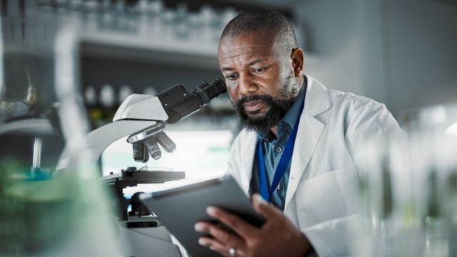 A scientist wearing a lab coat works in a lab with a microscope.