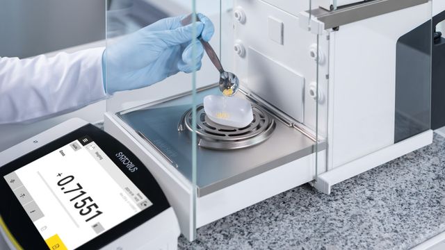 A technician using a precision balance to weigh powdered samples on a weighing boat, showcasing accurate measurements in a lab.