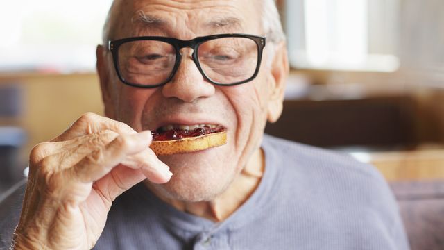 Older person eating jam on toast.
