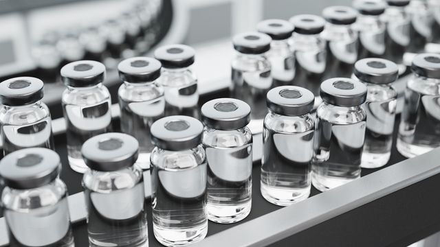Close-up view of multiple sterile vials filled with clear liquid, arranged in rows on a manufacturing line.
