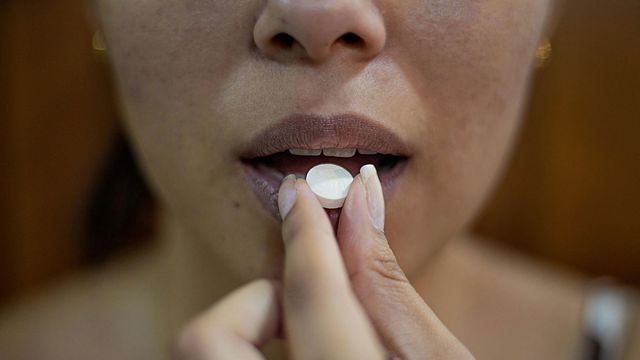 A person hold a white pill to their lips.