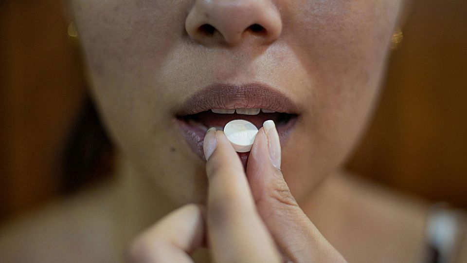 A person hold a white pill to their lips.