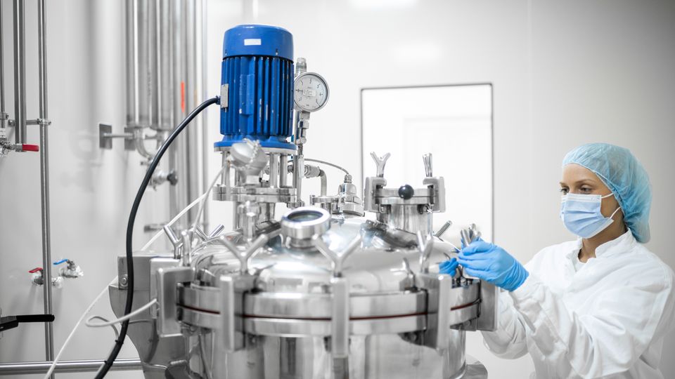 A female scientist in protective gear operates a bioreactor in a pharmaceutical bioprocessing facility.