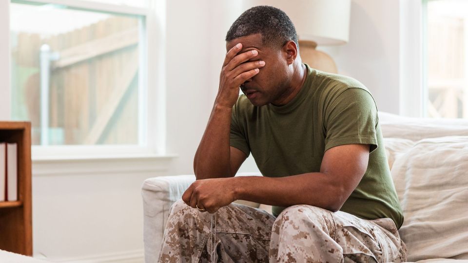 A soldier sitting on a couch with his head in his hands.